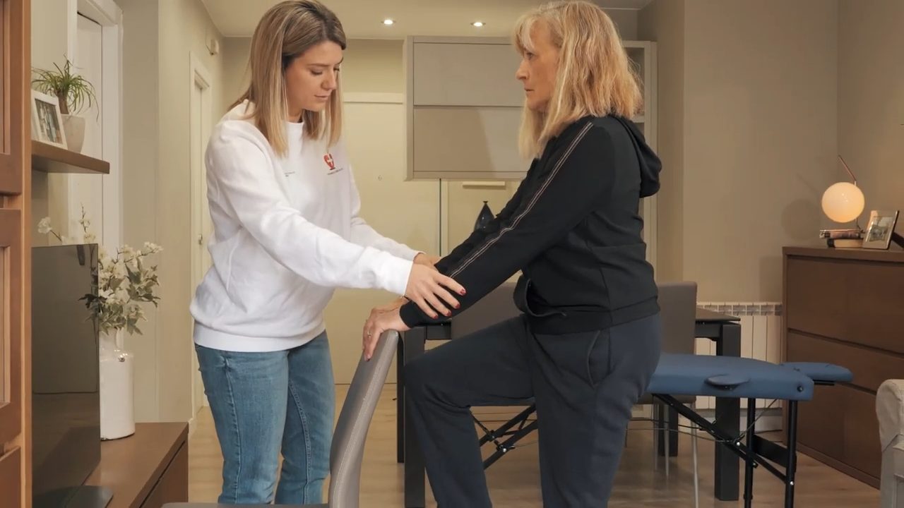 Fisioterapeuta ayudando a una persona mayor con ejercicios de equilibrio para la prevención de caídas en su domicilio de Barcelona.